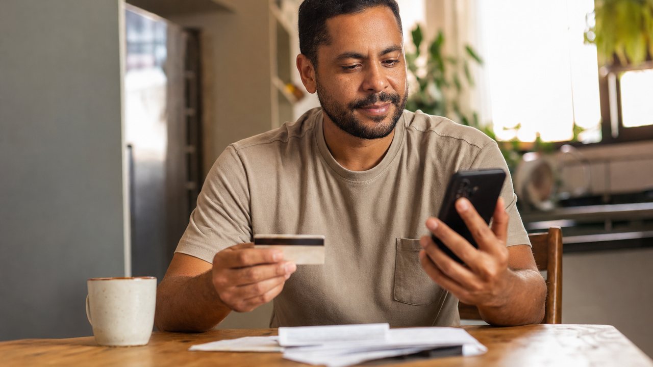 Homem brasileiro comparando cartão de crédito e Crédito do Trabalhador no celular em casa