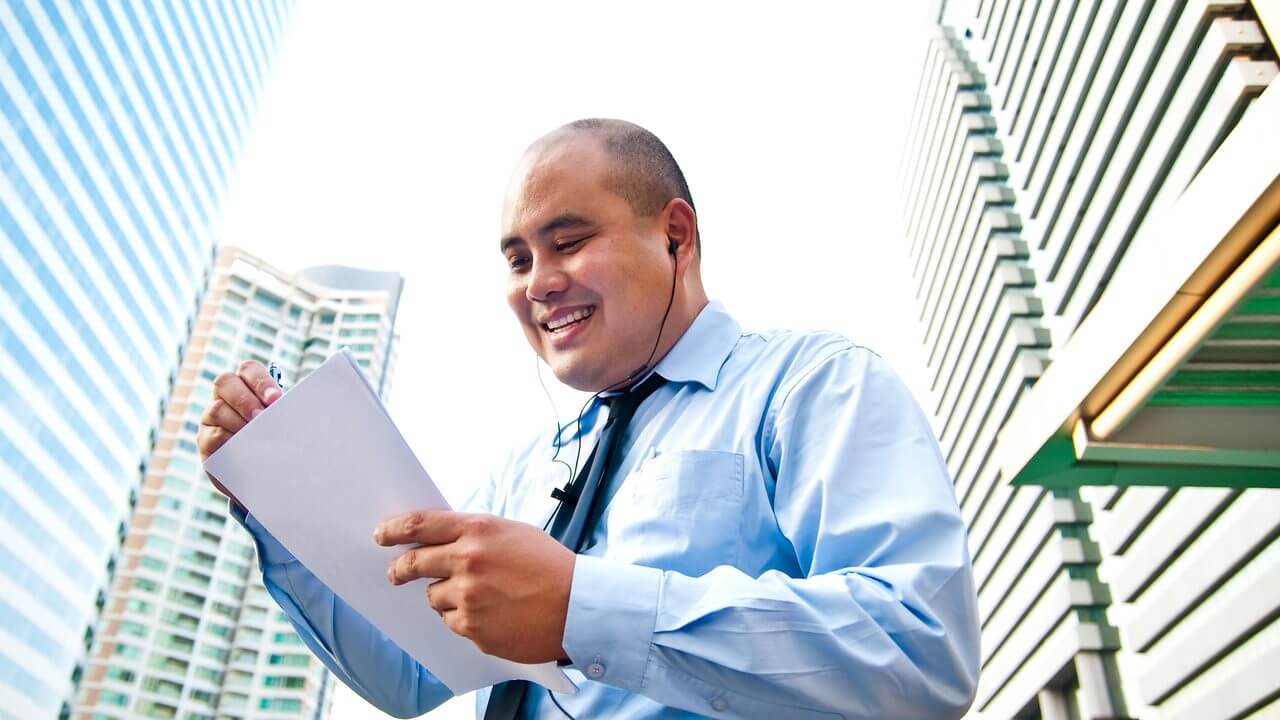 Trabalhador sorridente lê documentos entre prédios comerciais