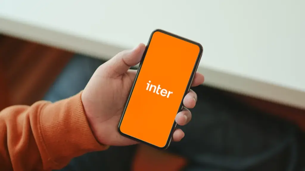 Mão segurando um celular com o logo do Inter em tela laranja.
