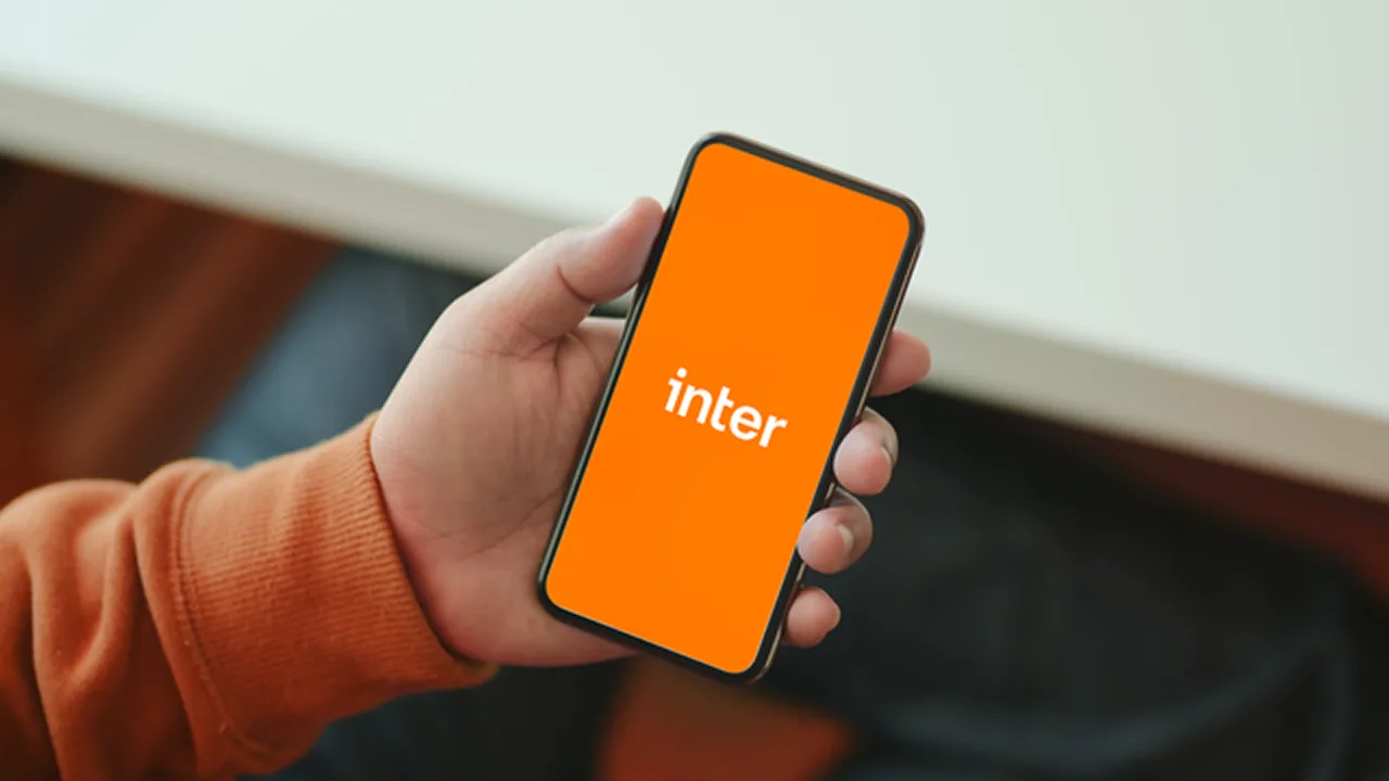 Mão segurando um celular com o logo do Inter em tela laranja.